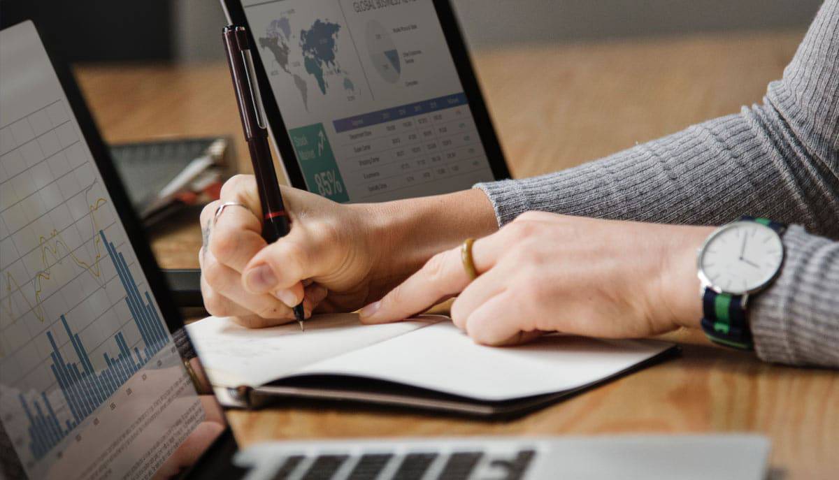 Banking Woman's hand working on financial reports with computers nearby.